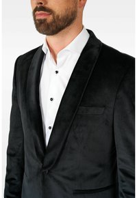 Črna žametna suknjič z satenskimi reverji, enojno gumbno zapiranje in bela srajca z črnimi gumbi. Gladka tekstura, prilagojen kroj.