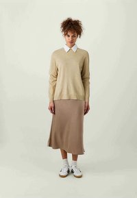 Beige knitted sweater with a white collared shirt underneath, paired with a light brown midi skirt and white sneakers with dark accents.