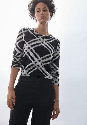 Maglione nero con motivo geometrico argento, colletto rotondo, maniche lunghe e una consistenza morbida. Abbinato a pantaloni neri sartoriali.