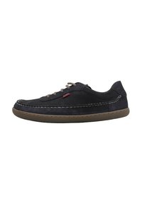 Zapatilla de cuero negro, punta redonda, suela de goma marrón contrastante, costuras decorativas y cordones marrones. La parte lateral presenta una etiqueta con el logo.