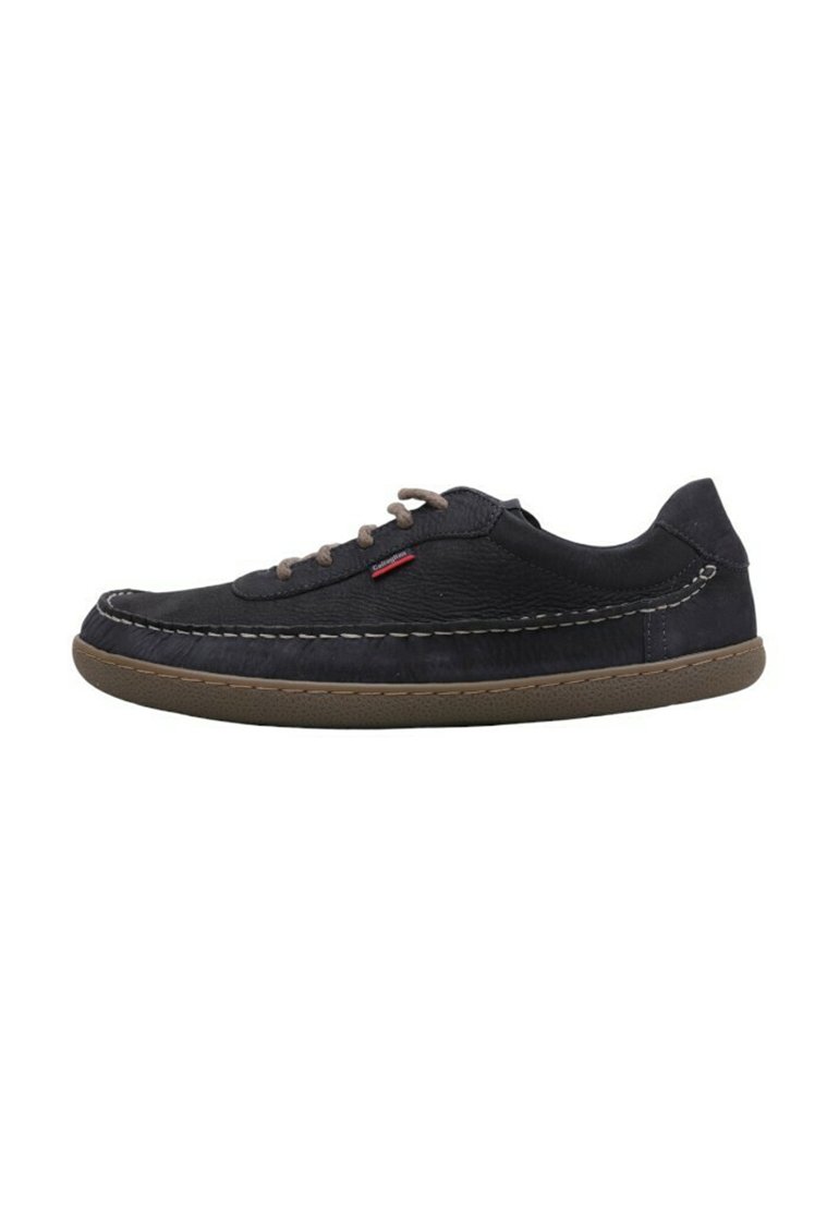 Zapatilla de cuero negro, punta redonda, suela de goma marrón contrastante, costuras decorativas y cordones marrones. La parte lateral presenta una etiqueta con el logo.