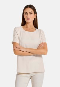 Kurzärmlige Bluse mit Rundhalsausschnitt in hellbeige, aus glattem Stoff mit lockerer Passform und geradem Saum. Einfaches, vielseitiges Design.