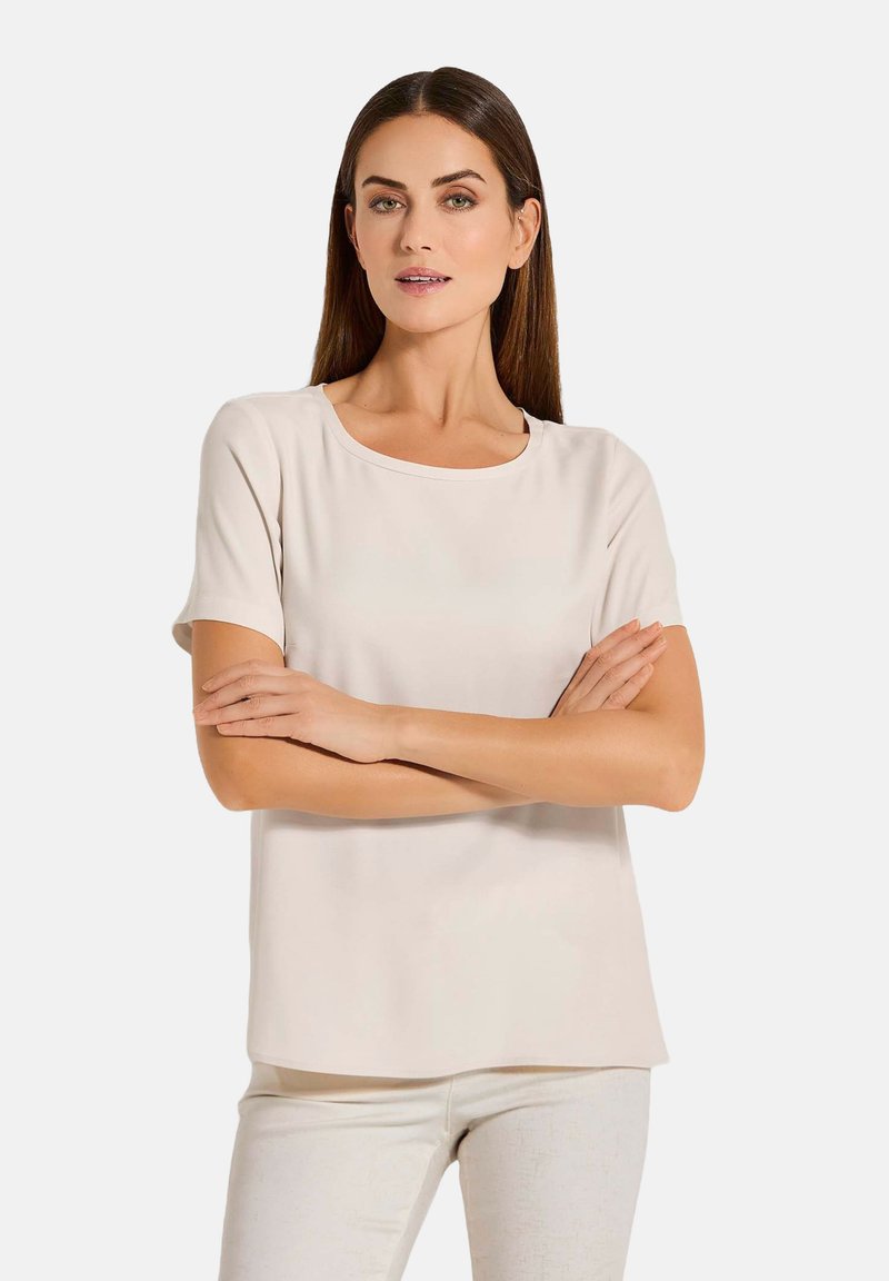 Kurzärmlige Bluse mit Rundhalsausschnitt in hellbeige, aus glattem Stoff mit lockerer Passform und geradem Saum. Einfaches, vielseitiges Design.