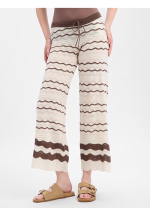 Cream and brown striped knit wide-leg pants with drawstring waist worn with tan studded slide sandals on model.