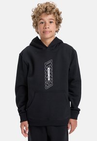 Čierna mikina s kapucňou, ktorá má predné kengurské vrecko, rebrované manžety a vertikálny biely potlač loga. Textúra tkaniny sa zdá byť mäkká a hrubá.