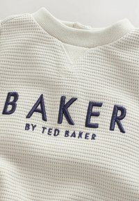 Pull en maille blanc avec un col côtelé ; présente le texte brodé en bleu marine "BAKER" et "by TED BAKER" affiché en évidence.