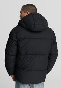 Czarna kurtka puchowa z kapturem, charakteryzująca się pikowanym wzorem i teksturowanym wykończeniem. Tył jest nieco dłuższy i ma luźny krój.