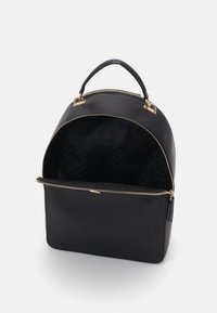 Schwarzer Leder-Rucksack mit abgerundetem Oberteil, goldfarbenem Reißverschluss und einem Innenraum, der mit einem dezenten Musterstoff ausgekleidet ist. Fächerdesign.