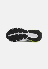 La semelle de chaussure présente une base en caoutchouc noir avec des rainures profondes et texturées pour une adhérence, accentuée par une semelle intermédiaire blanche et des détails en jaune vif.