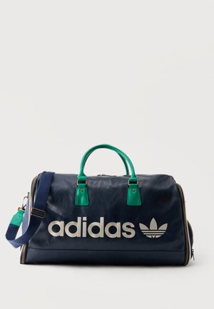 Tmavomodrá Adidas taška s zelenými rukoväťami, nastaviteľným ramenným popruhom a veľkým bielym logom Adidas na prednej strane.