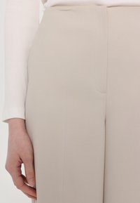 Beige op maat gemaakte broeken van een gladde, gestructureerde stof met een rechte voorkant, voorzien van zijzakken en een schone, minimalistische afwerking.