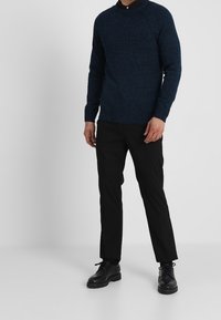 Marinblå stickad tröja med rund hals och raglanärmar, i kombination med svarta slim-fit byxor och svarta snörskor.