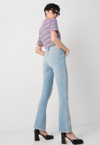 Jeans de cintura alta de color azul claro con pierna acampanada, combinados con una blusa de manga corta a rayas de múltiples colores y zapatos de tacón cuadrado negros.