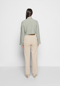Chaqueta verde claro texturizada y recortada con mangas largas, combinada con pantalones beige de cintura alta y tacones altos beige claros.