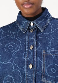 Niebieska koszula denimowa z kwiatowym wzorem, z kołnierzykiem, metalowymi guzikami i kieszenią na piersi, z kontrastowymi detalami przeszyć.