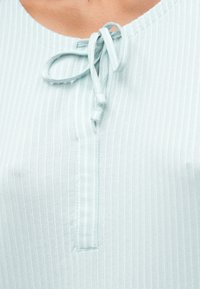 Κοντινό πλάνο από τον λαιμό ενός ανοιχτού μπλε ριπ σέτ με μια δεμένη κορδέλα φτιαγμένη από κομμάτια υφάσματος.