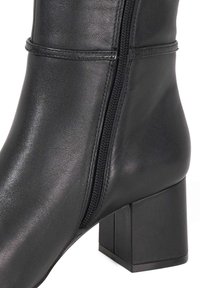 Black leather ankle boot featuring a square block heel, side zipper, smooth texture, and subtle stitching details along the shaft.