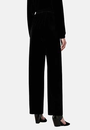 Pantaloni di velluto nero con vestibilità rilassata, caratterizzati da una vita elasticizzata e gambe larghe, abbinati a tacchi neri.