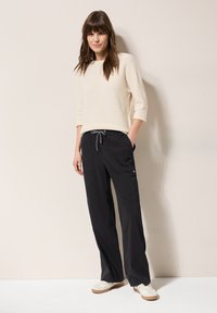 Cream knit sweater with three-quarter sleeves paired with loose-fitting black trousers featuring drawstring waist and side pockets.