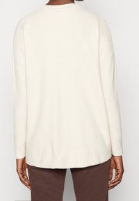 Pull beige en maille avec une coupe décontractée, texture côtelée et ourlet arrondi. Manches longues et encolure ras du cou. Design minimaliste.
