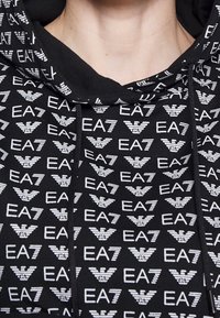 Czarna bluza z kapturem z powtarzającym się białym wzorem logo EA7. Posiada kaptur z regulowanym sznurkiem i miękką fakturę, zaprojektowana do codziennego noszenia.