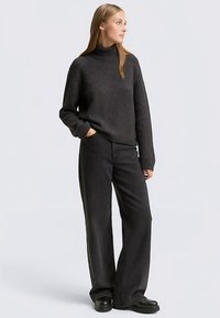 Pull tricoté gris foncé avec manches côtelées et col montant, associé à un jean noir à jambes larges et des bottes noires épaisses. Design simple et moderne.