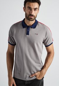 Szara koszulka polo z granatowym kołnierzykiem i mankietami, czerwonymi paskami na ramionach oraz małym logo na piersi, wykonana z gładkiego bawełnianego materiału.