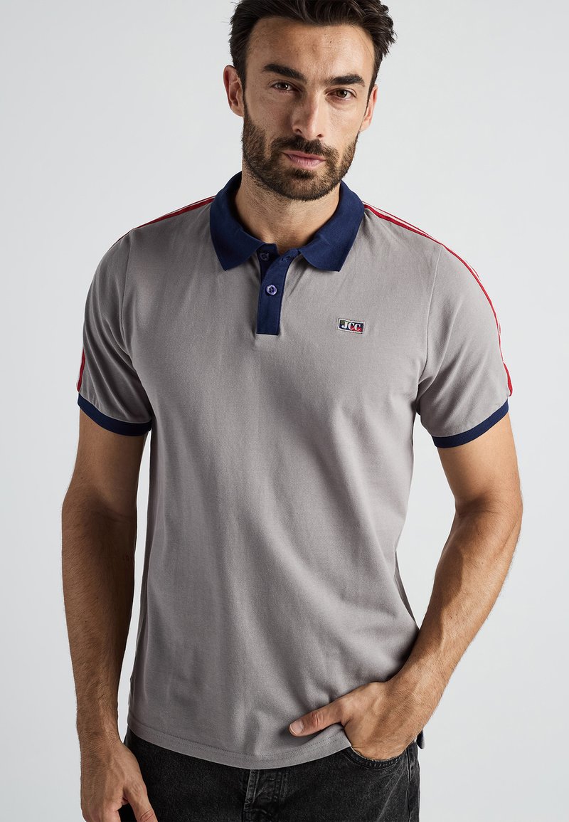 Szara koszulka polo z granatowym kołnierzykiem i mankietami, czerwonymi paskami na ramionach oraz małym logo na piersi, wykonana z gładkiego bawełnianego materiału.