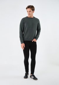 Sudadera gris oscuro con cuello redondo, puños y cintura acanalados, combinada con jeans negros ajustados y zapatillas deportivas negras.