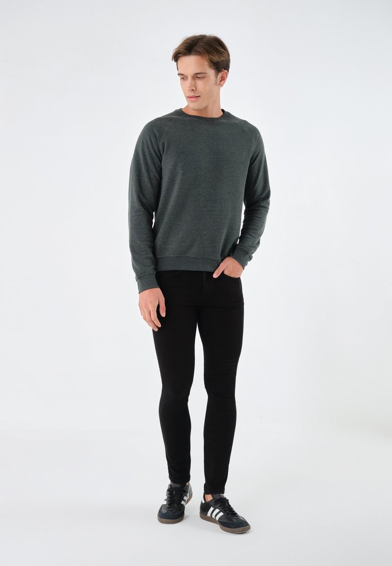 Sudadera gris oscuro con cuello redondo, puños y cintura acanalados, combinada con jeans negros ajustados y zapatillas deportivas negras.