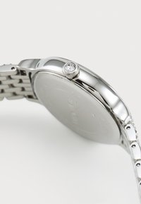 Silver metal wristwatch with a round case, textured crown featuring a clear gemstone, and a linked bracelet design.