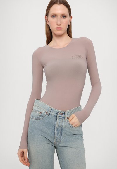 Langärmliger Body aus weichem Mauve-Stoff, mit Rundhalsausschnitt und minimalistischem Druck nahe der Schulter, kombiniert mit hochtaillierten Jeans.