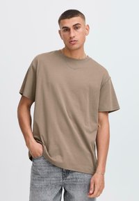 Camiseta corta de manga corta en color marrón, hecha de algodón y con un corte relajado. Presenta un escote redondo y una textura suave. Combinada con jeans de color gris claro.