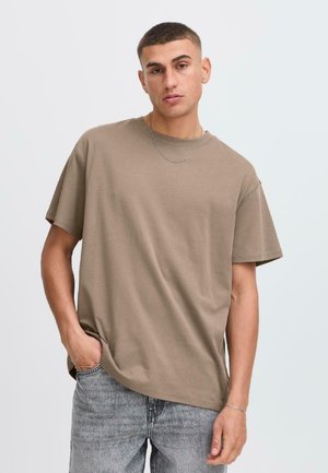 Braunes Kurzarm-T-Shirt aus Baumwolle mit lockerer Passform. Hat einen runden Halsausschnitt und eine glatte Textur. Kombiniert mit hellgrauen Jeans.