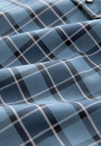 Blau kariertes Stoffmuster mit verschiedenen Blautönen sowie schwarzen und weißen Linien. Die Textur ist glatt und zeigt ein gewebtes Muster mit fallenden Falten.