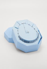 Silberne Kettenhalskette mit blauen, runden Edelsteinen, die in einer sechseckigen, hellblauen Box mit strukturierter Oberfläche liegt.