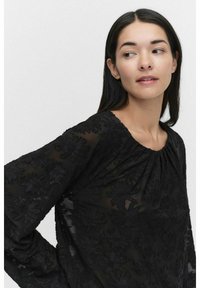 Svart broderad blus med genomskinlig textur, rund halsringning och långa ärmar med blommönster. Tyget är designat för lätt och bekväm användning.