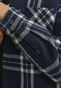 Tamsiai mėlynas ir baltas languotas flanelinis marškinis su mygtukų reguliuojamais rankovėmis, pasižymintis minkšta tekstūra ir kišenės detalėmis, demonstruojantis languotą raštą.