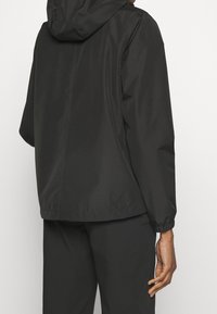 Svart, vattentät jacka med huva, elastiska ärmslut och lös passform. Slät yta utan framträdande mönster eller hårdvarudetaljer.