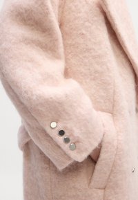Casaco longo de lã rosa com um acabamento texturado e felpudo. Apresenta botões prateados nas mangas e um design ajustado.