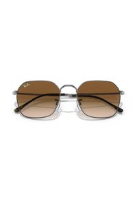 Occhiali da sole Ray-Ban con lenti grigio marrone a sfumatura, forma rettangolare, montatura in plastica trasparente, dettagli argentati e punte scure delle aste.