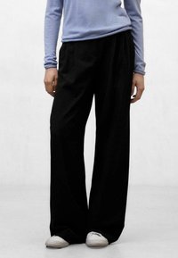 Pantalones negros de pierna ancha con un ajuste relajado, cintura alta y textura suave. Combinados con una camisa de manga larga azul claro y zapatos blancos.