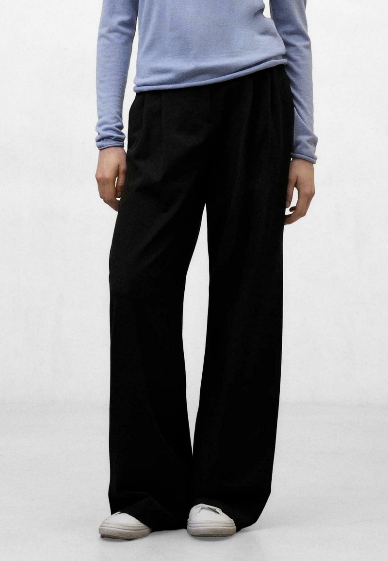 Pantalones negros de pierna ancha con un ajuste relajado, cintura alta y textura suave. Combinados con una camisa de manga larga azul claro y zapatos blancos.