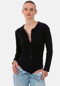 Body noir à manches longues côtelé avec col et patte de boutonnage ; le modèle porte un jean bleu clair déboutonné. Texture lisse.