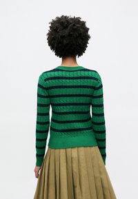 Πλεκτό πουλόβερ με πράσινες και ναυτικές ρίγες, με υφή πλέξης και ριμπ μανσέτες. Το σχέδιο περιλαμβάνει στρογγυλή λαιμόκοψη και εφαρμοστή μέση.