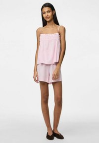 Rosa ärmlös topp med volangkant och matchande shorts, med en mjuk yta och avslappnad silhuett. Bruna slip-on skor.