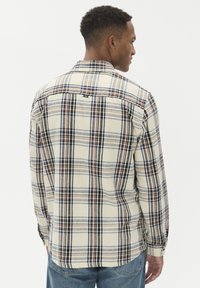 Moška flanelasta srajca v kremni barvi z mornarsko modrim, rjavim in sivo karirastim vzorcem. Ima dolge rokave, gumbe na zapestjih in detajl jermena na hrbtu.