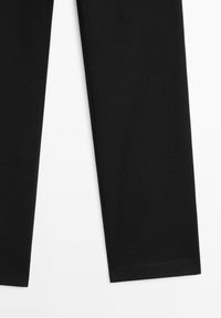 Partie inférieure d'un pantalon noir à jambe droite sur fond blanc, montrant des ourlets nets et une texture de tissu lisse.