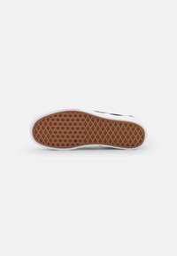White sneaker sole featuring a textured brown rubber bottom with a honeycomb pattern for traction. Minimalist design with clean lines.