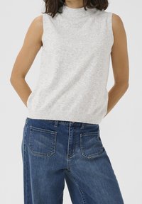 Maglione senza maniche grigio chiaro con collo alto, realizzato in tessuto morbido. Abbinato a jeans a vita alta blu scuro con tasche posteriori.